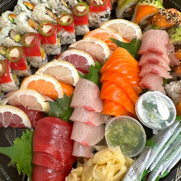 A vibrant sushi platter with various rolls, sashimi, citrus slices, ginger, wasabi, and soy sauce packets.