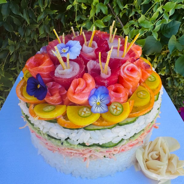A vibrant sushi cake with layers of rice, fish, and vegetables, garnished with edible flowers.