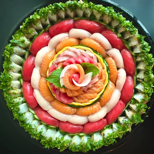 A large, circular sushi platter with various colorful nigiri, sashimi, and maki rolls.