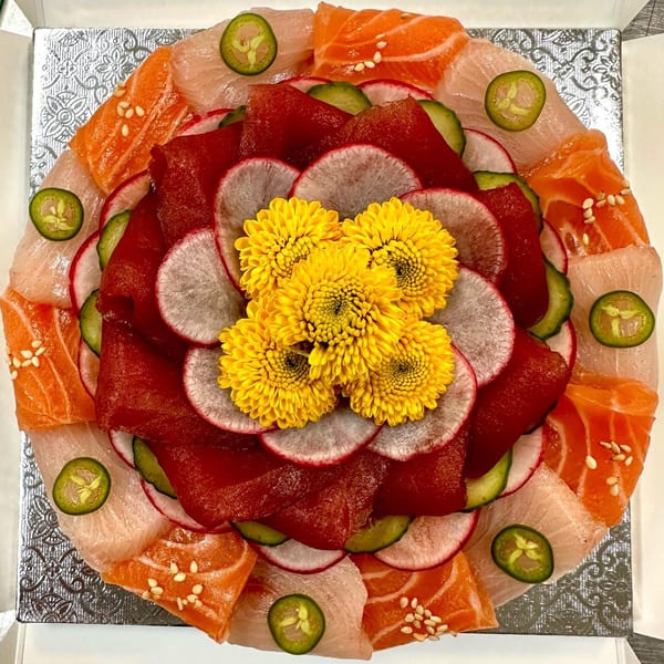 Sushi Friend's sashimi platter with salmon, tuna, radishes, cucumbers, jalapeños, and yellow flowers.