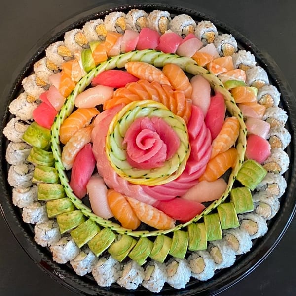 A large, circular sushi platter with a tuna and cucumber rose centerpiece, surrounded by various rolls and sashimi.