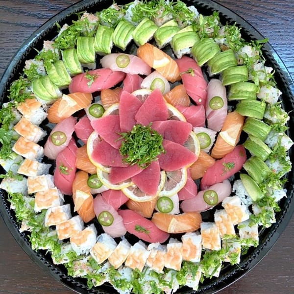 A large platter of Sushi Friend's colorful sushi, sashimi, and rolls, garnished with avocado, lemon, and jalapeño.