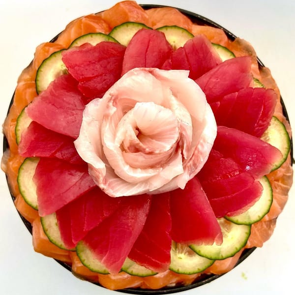 Overhead view of a sushi cake with salmon, tuna, cucumber, and a white fish rose.